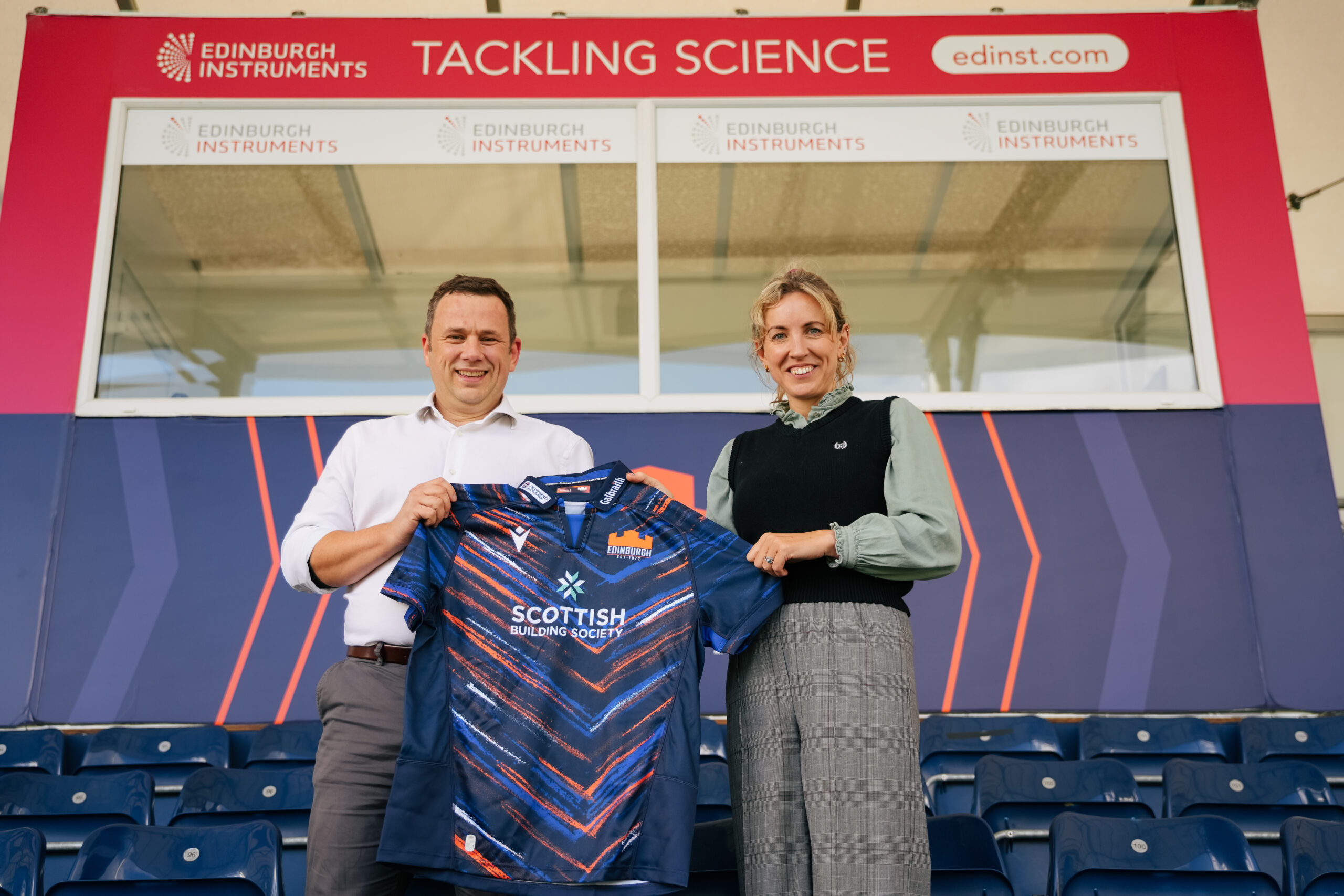 Roger Fenske and CJ hold Edinburgh Rugby shirt infront of Tackling Science coach box. 